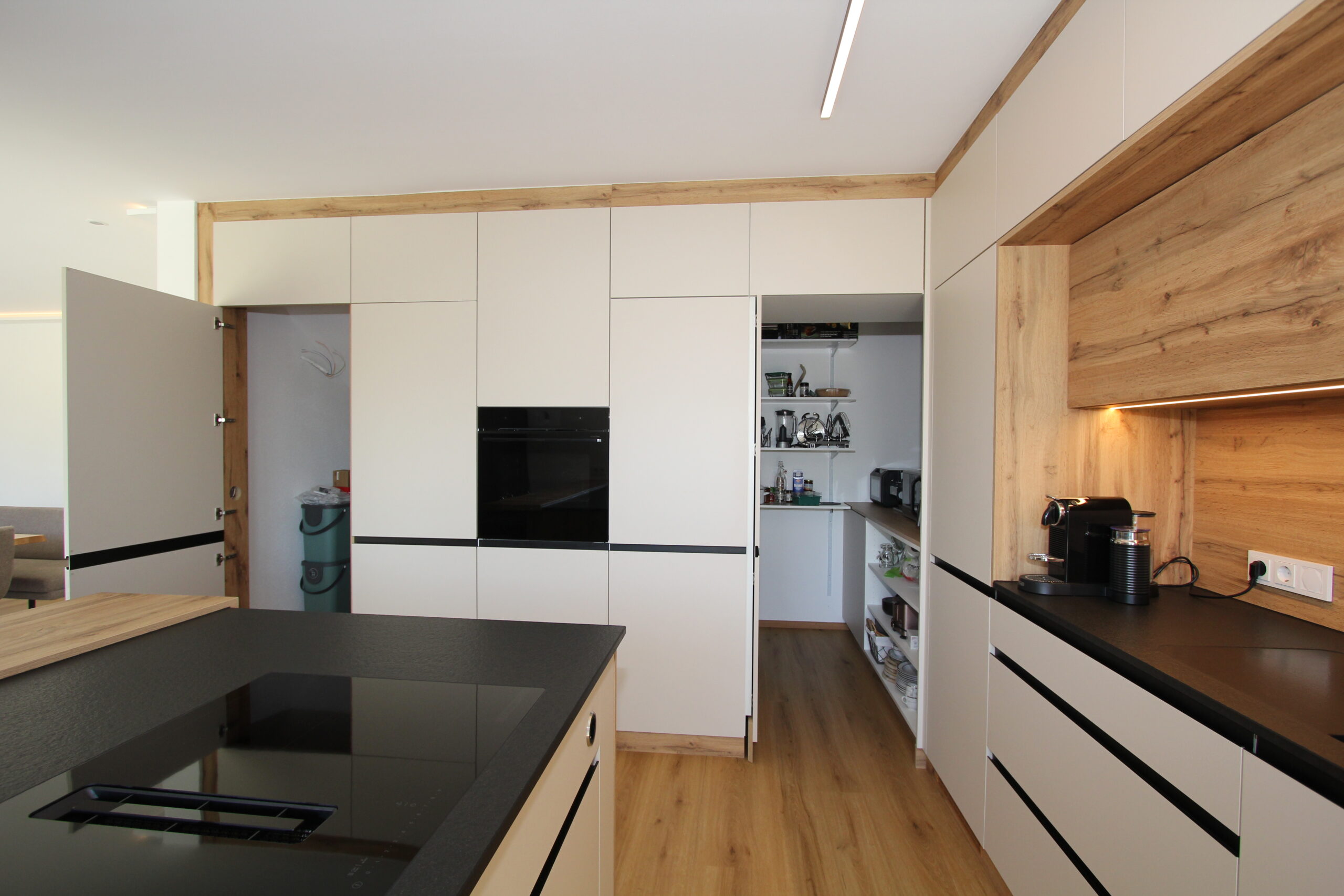 Küche in Beige und Wildeiche mit integrierter Speis, Dampfbackofen und Kochinsel mit Muldenlüfter