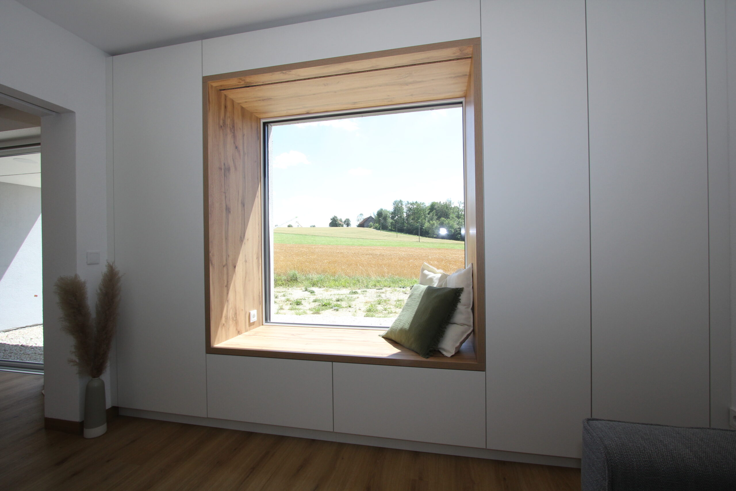 In den Schrankverbau integriertes Sitzfenster aus Eiche mit Ausblick ins Grüne im Wohnzimmer