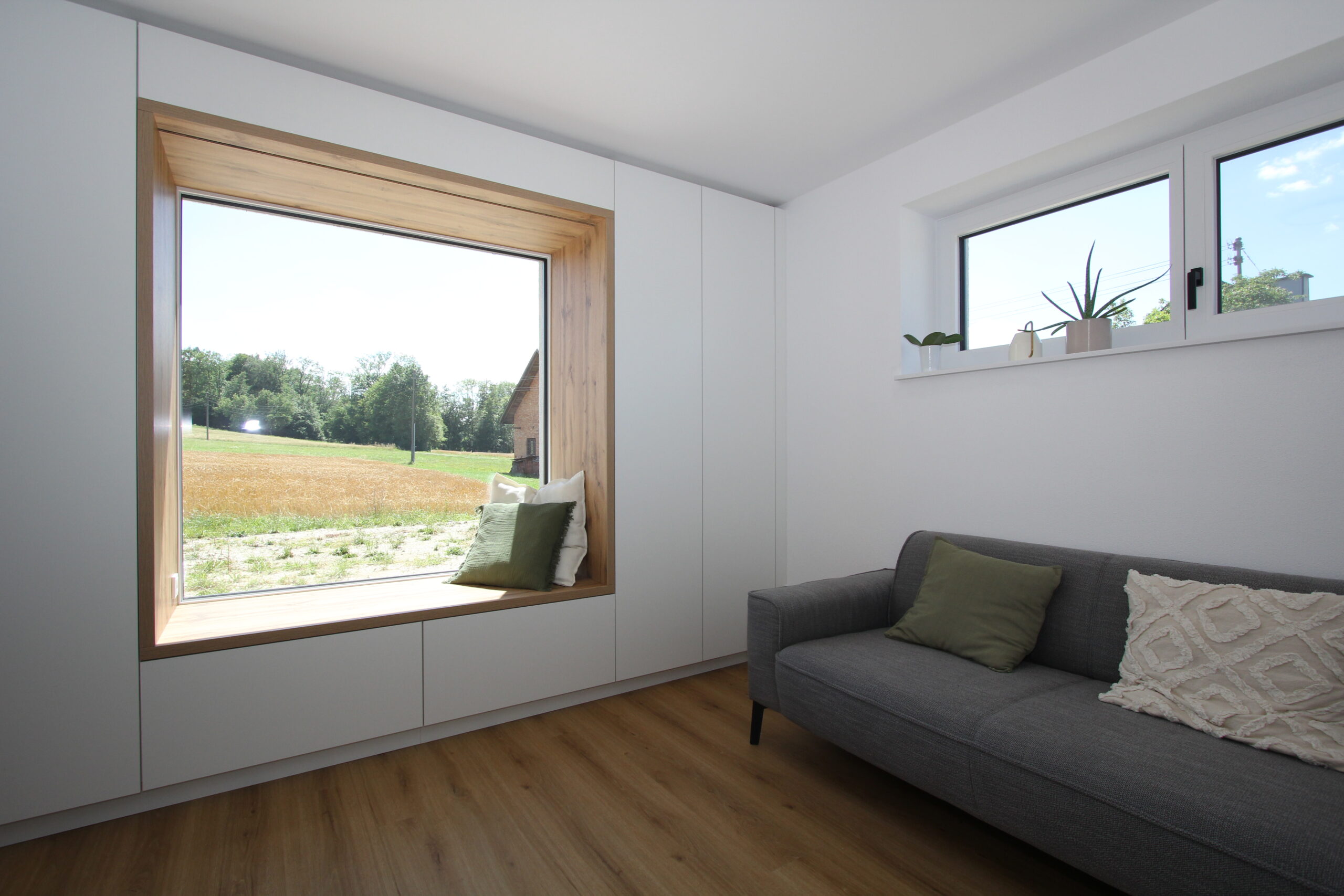 In den Schrankverbau integriertes Sitzfenster aus Eiche mit Ausblick ins Grüne im Wohnzimmer